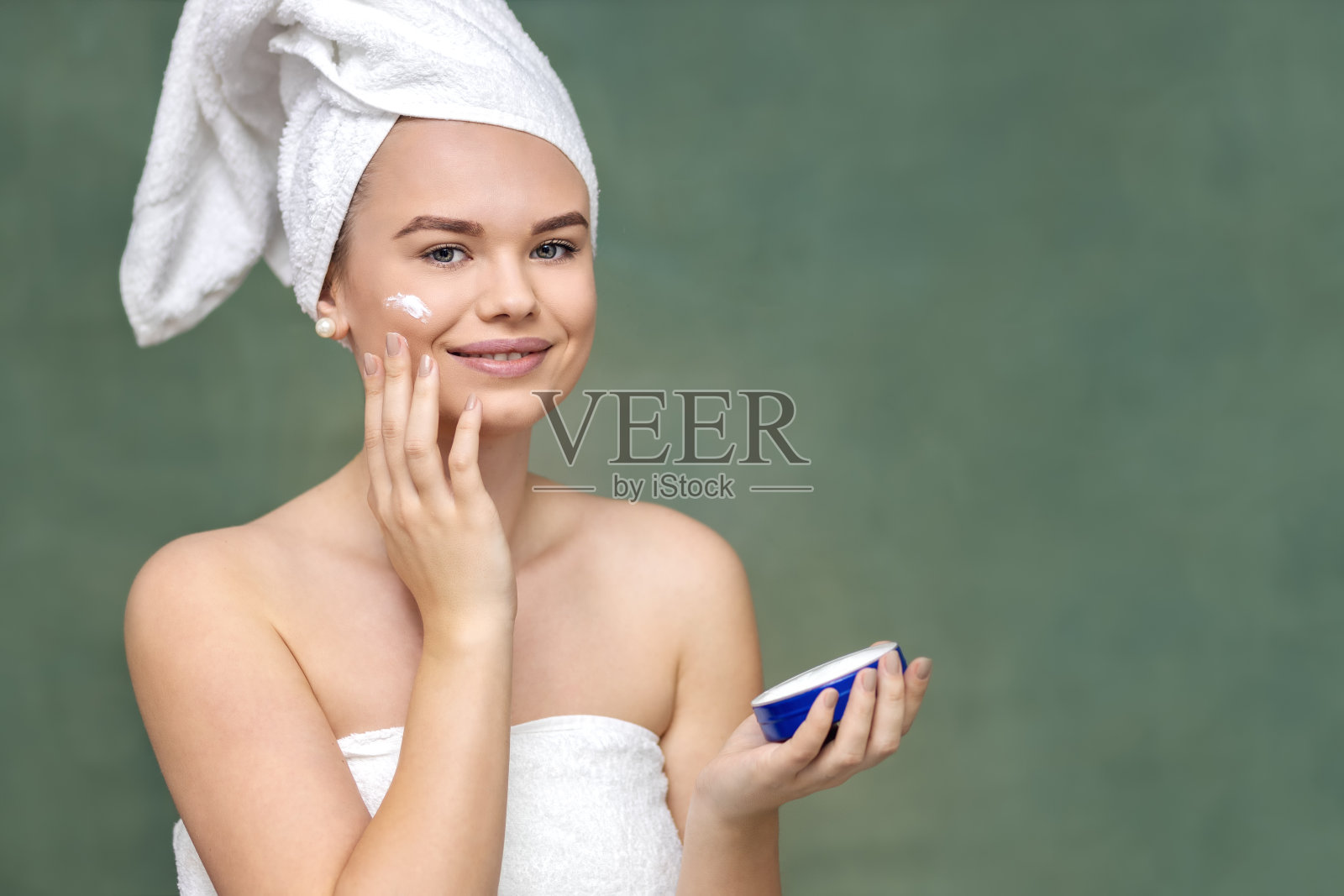 微笑的年轻女子在脸上涂抹保湿霜，使皮肤健康照片摄影图片