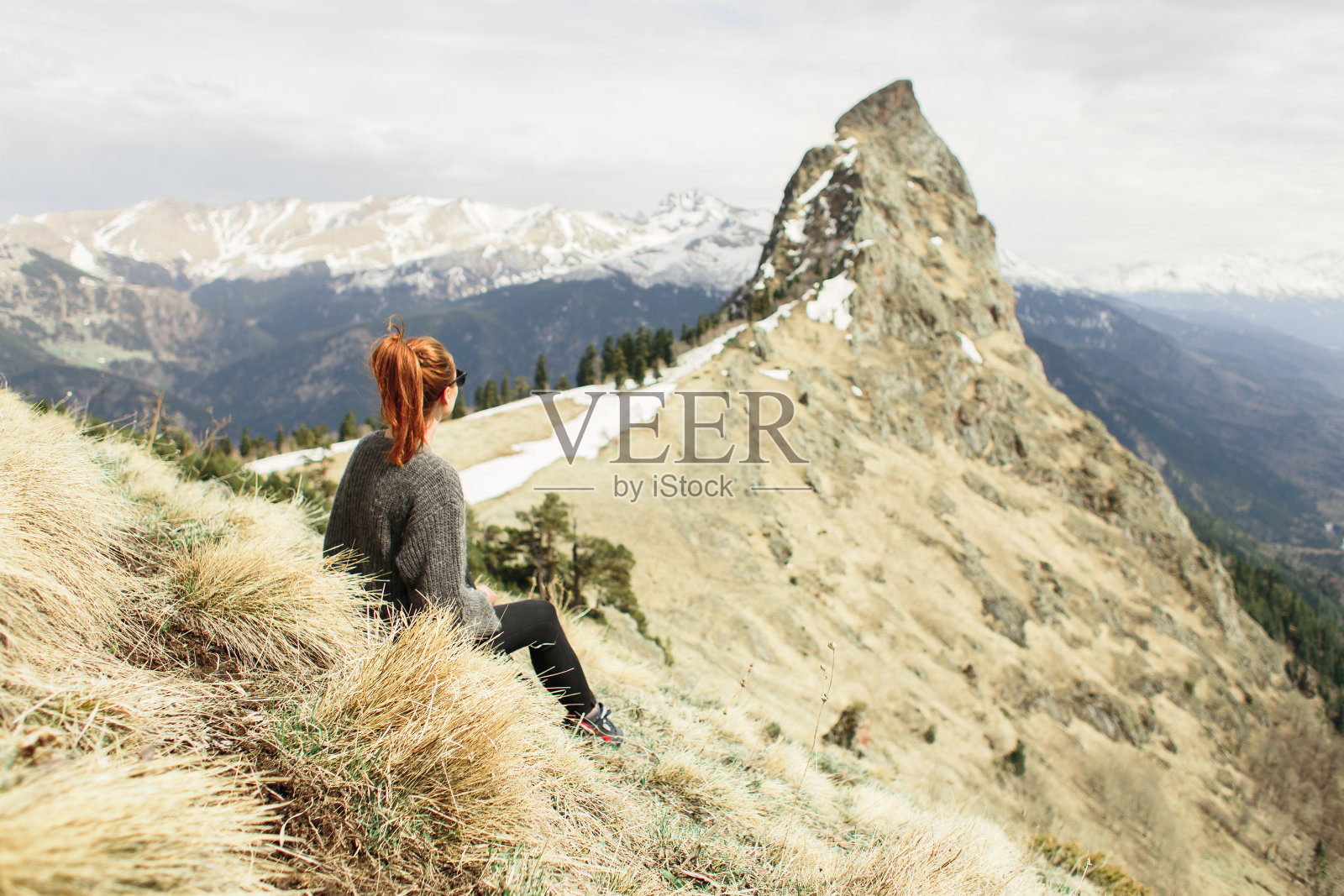 一个年轻的女孩坐在草地上，看着山顶照片摄影图片