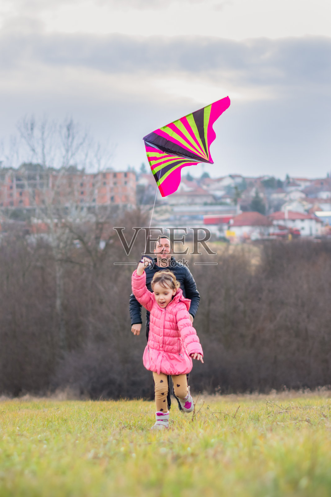 父亲和女儿带着风筝在草地上奔跑。照片摄影图片