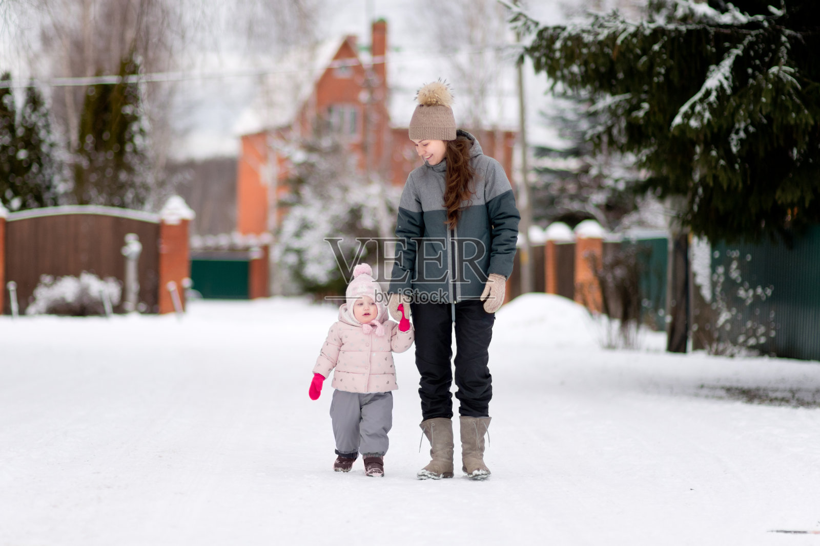 一位年轻的母亲和她的小女儿在一个白雪覆盖的村庄里散步照片摄影图片