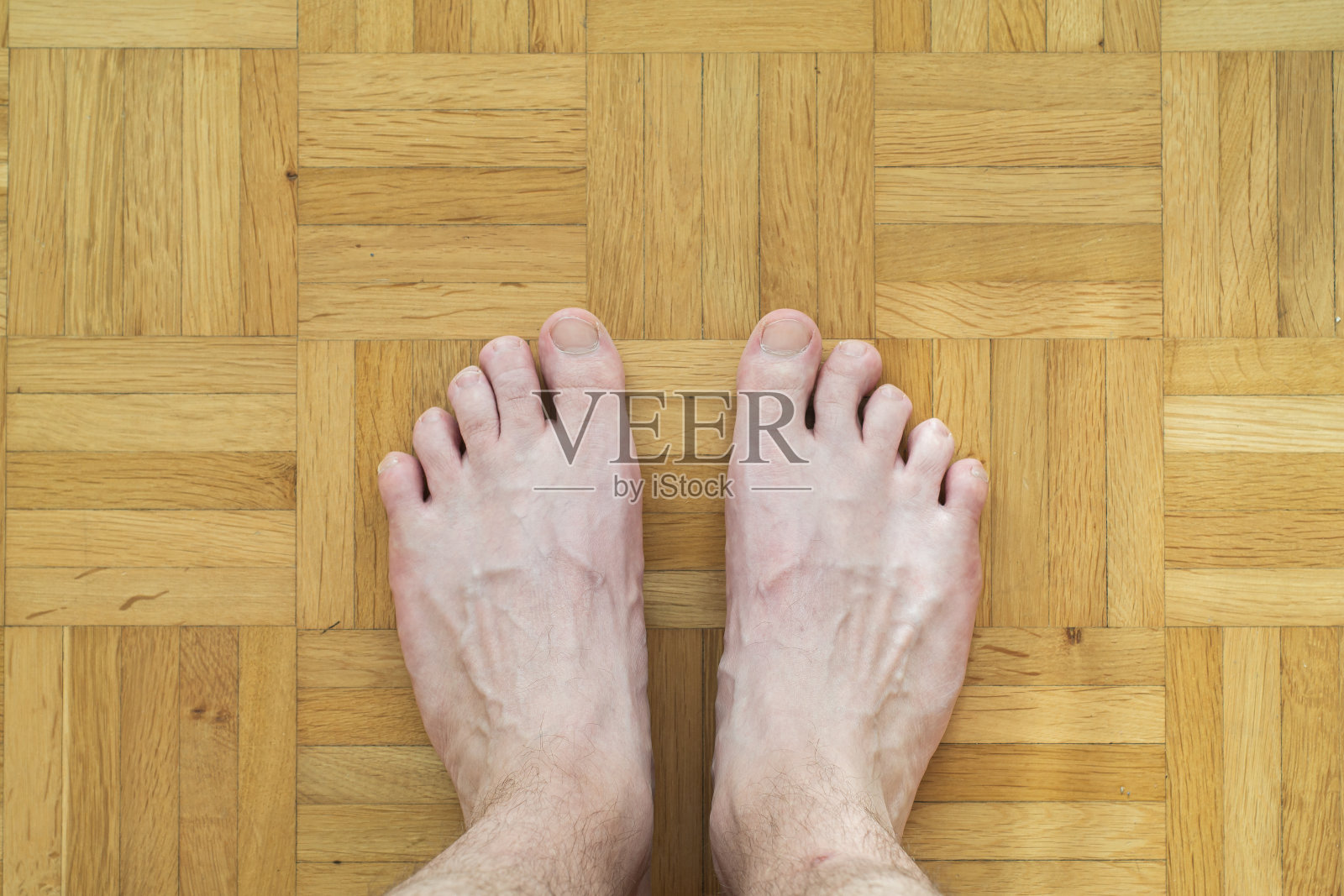 白种人男性光脚与弯曲的脚趾手指站在木质瓷砖地板上俯视体毛照片摄影图片