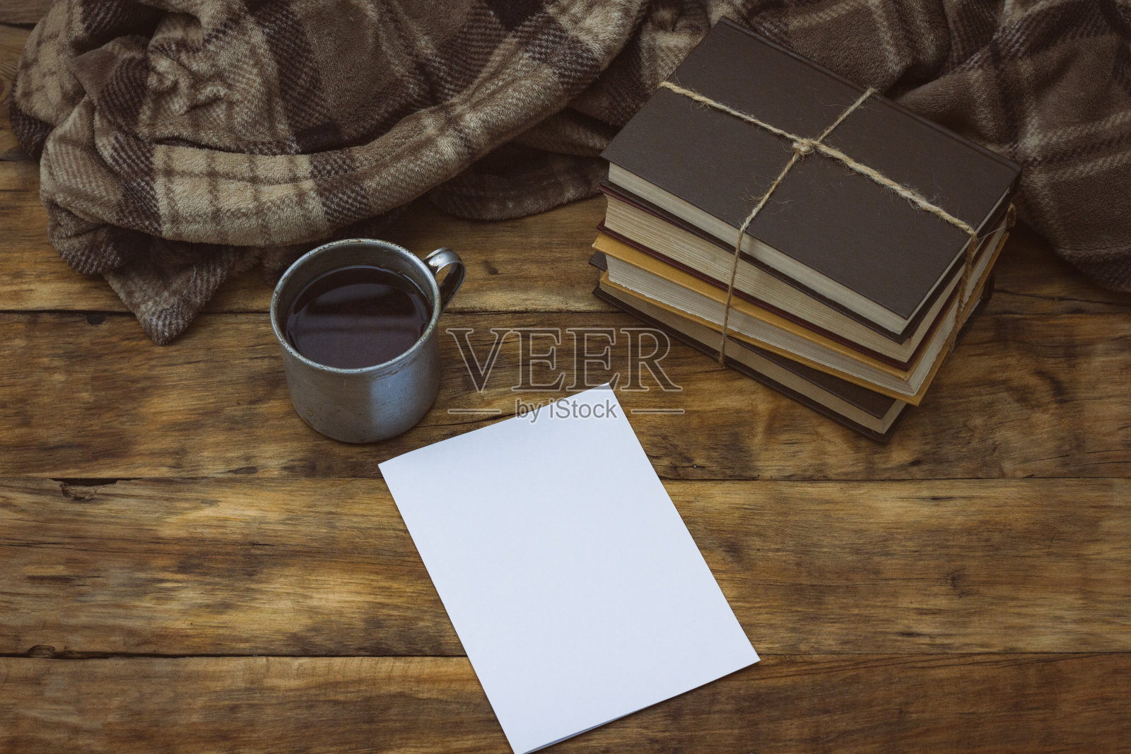 木桌上放着一张纸、一本书、一个放着咖啡的铝制古董杯和一条毯子。照片摄影图片