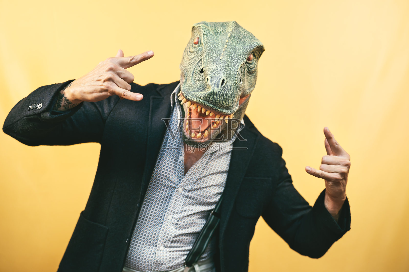 戴着霸王龙恐龙面具的老男人-疯狂的嬉皮士在庆祝狂欢节假日-荒谬和超现实的有趣概念-黄色背景照片摄影图片