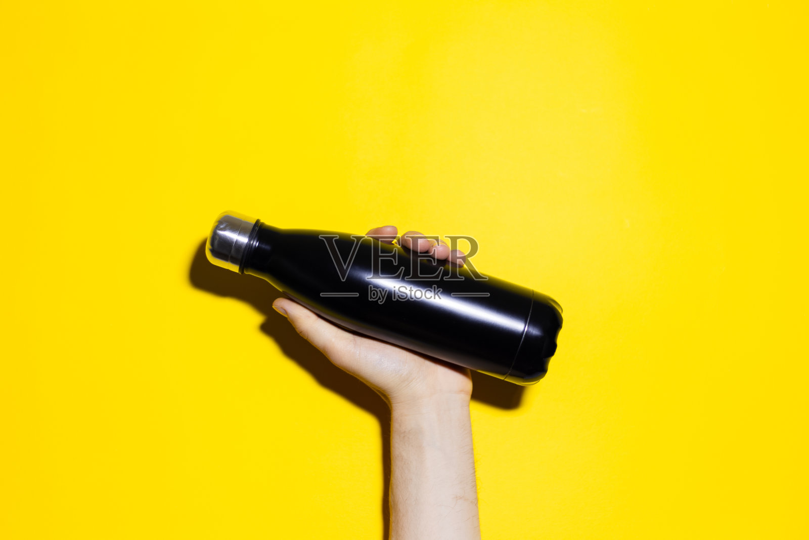 男性手握可重复使用的黑色钢质热水瓶的特写。孤立在黄色背景上。照片摄影图片
