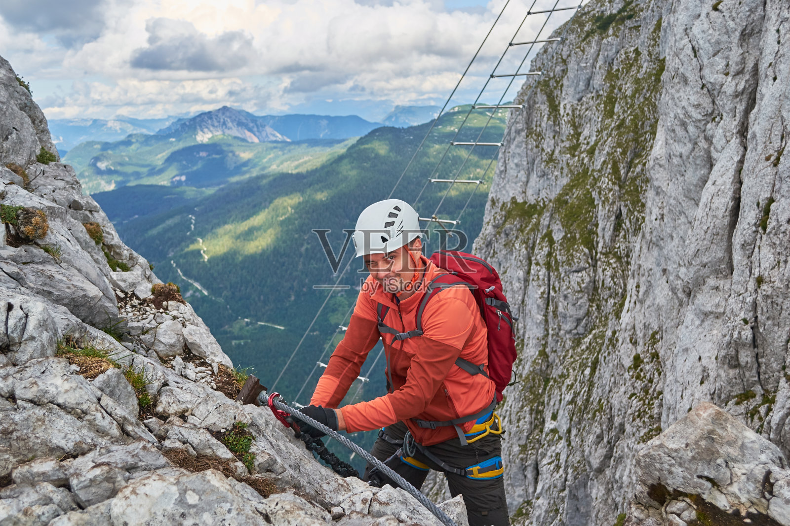 攀登者对着镜头眨着眼睛，同时在奥地利的Donnerkogel山的ferrata Intersport上更换吊带。照片摄影图片