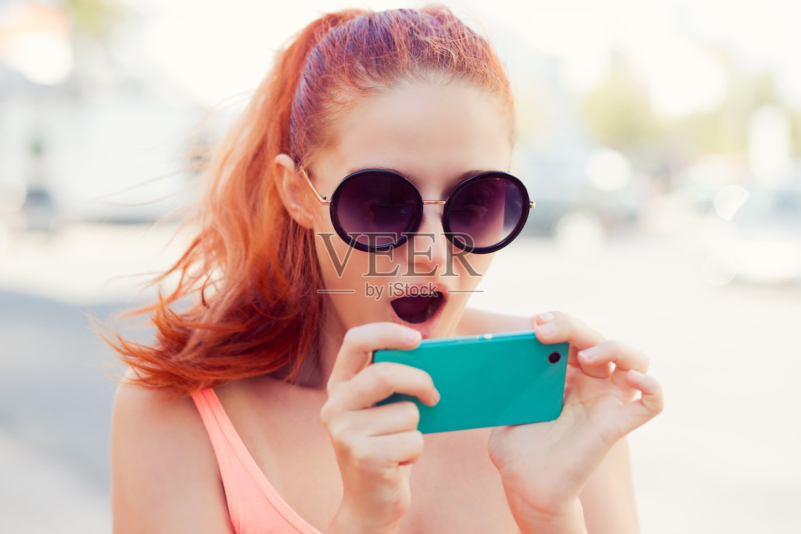 短信。特写肖像滑稽震惊年轻红头发的女孩女人看手机看到令人惊讶的新闻照片信息与补偿的情绪在城市景观背景上的脸照片摄影图片