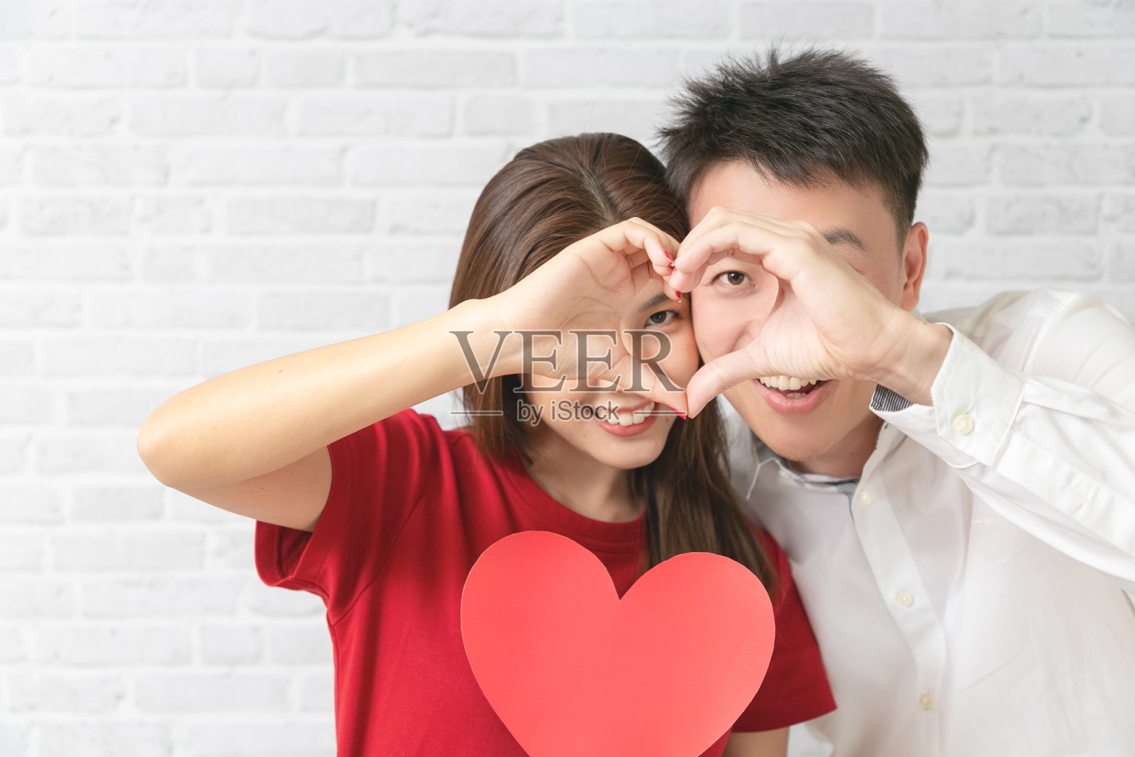 一对年轻夫妇正在做心形手势，微笑着看着镜头。情人节的概念。照片摄影图片