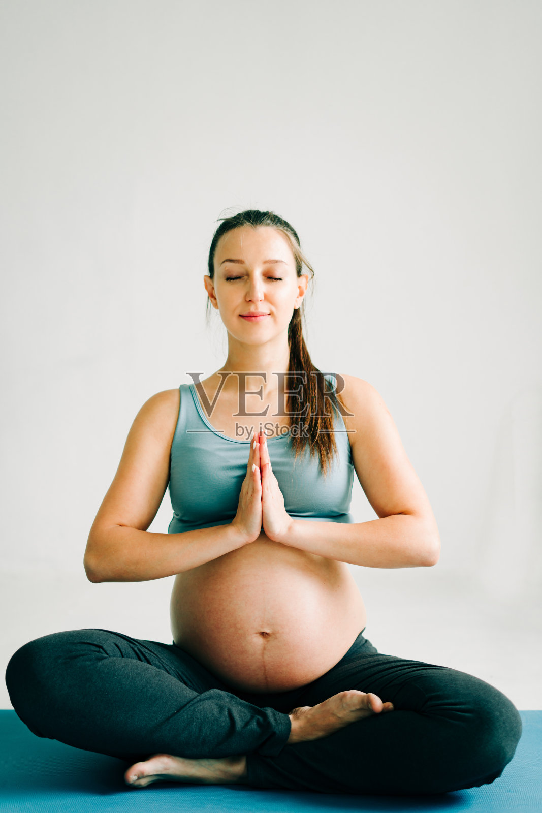 一个年轻美丽的怀孕女孩穿着运动服，坐在地毯上练习瑜伽照片摄影图片