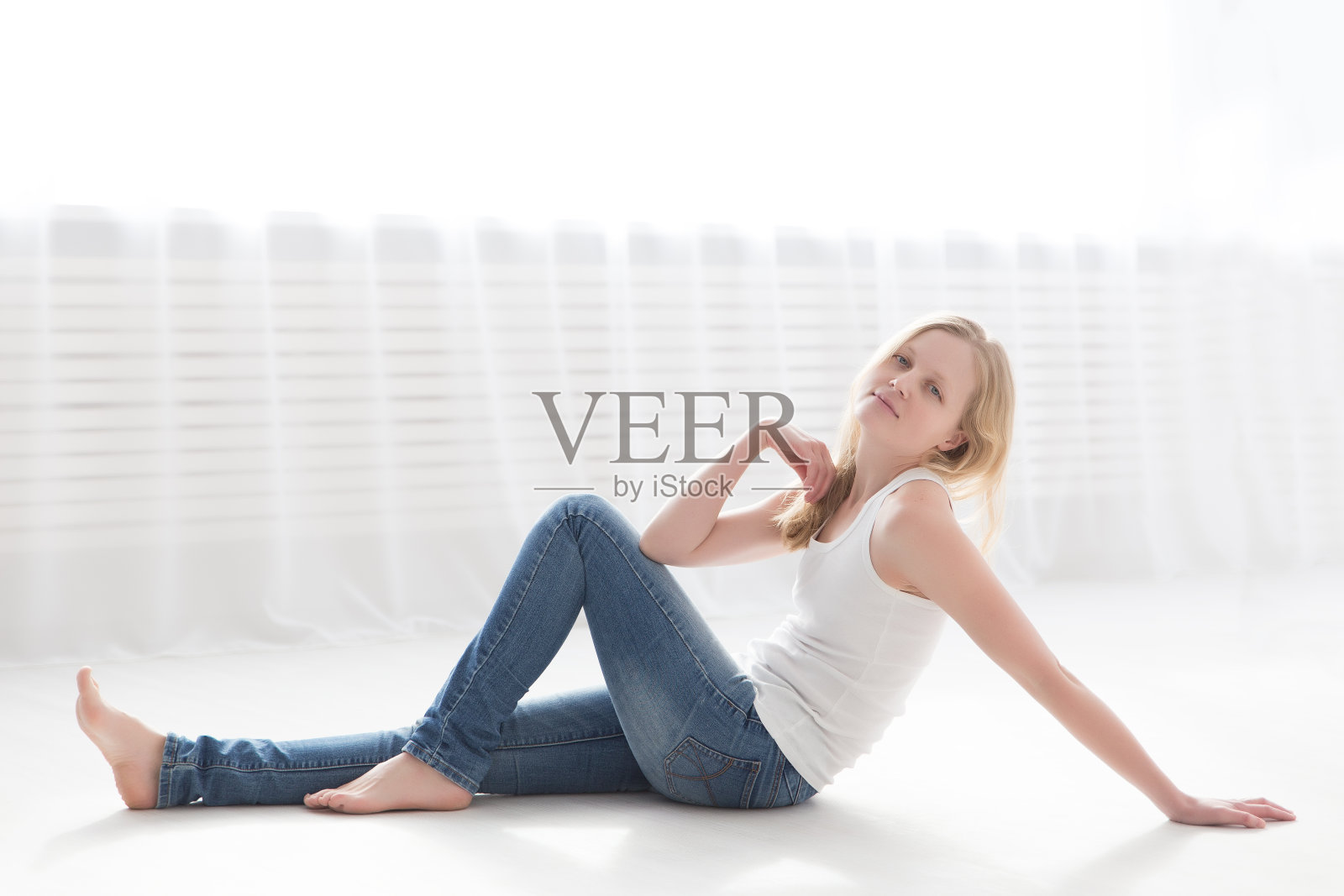在一个明亮的房间里，一个穿着牛仔裤和白色t恤的金发美女躺在地板上照片摄影图片