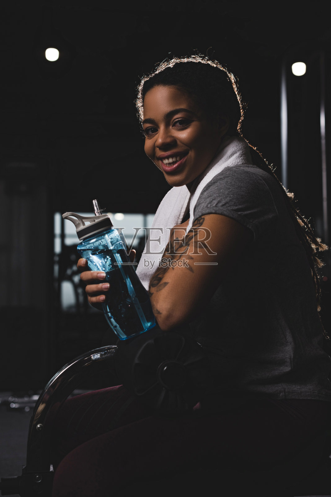 快乐的非裔美国女孩纹身拿着运动瓶在健身房照片摄影图片