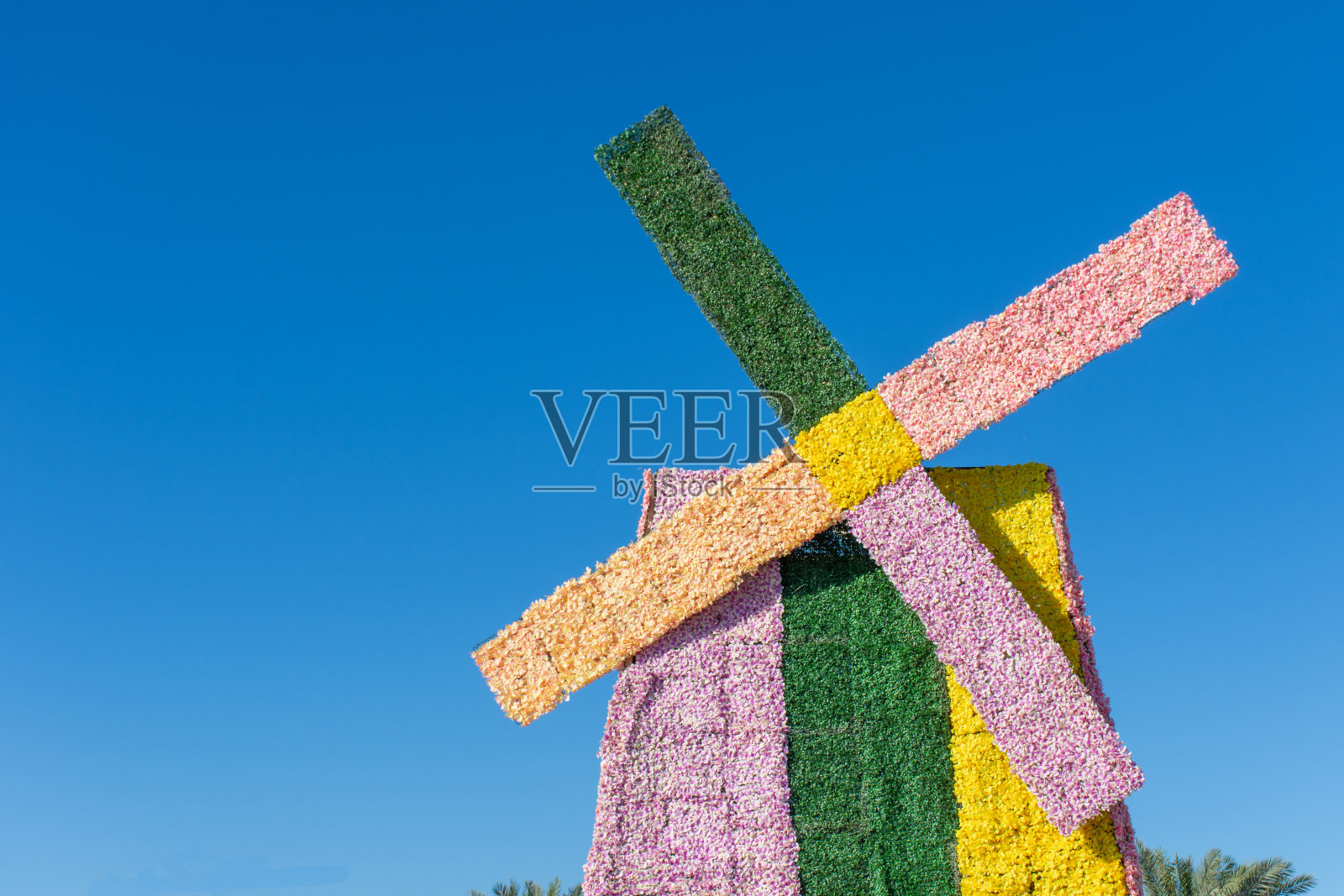 在晴朗的蓝天下，一个花风车被涂上了粉色、绿色和黄色。荷兰或荷兰主题或概念。照片摄影图片