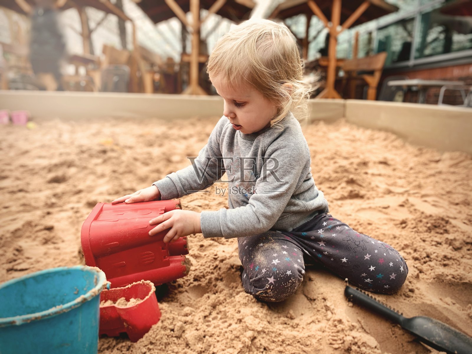 小女孩在沙盒里建沙堡-多民族的小女孩在操场上玩塑料勺和水桶在沙盒里。照片摄影图片