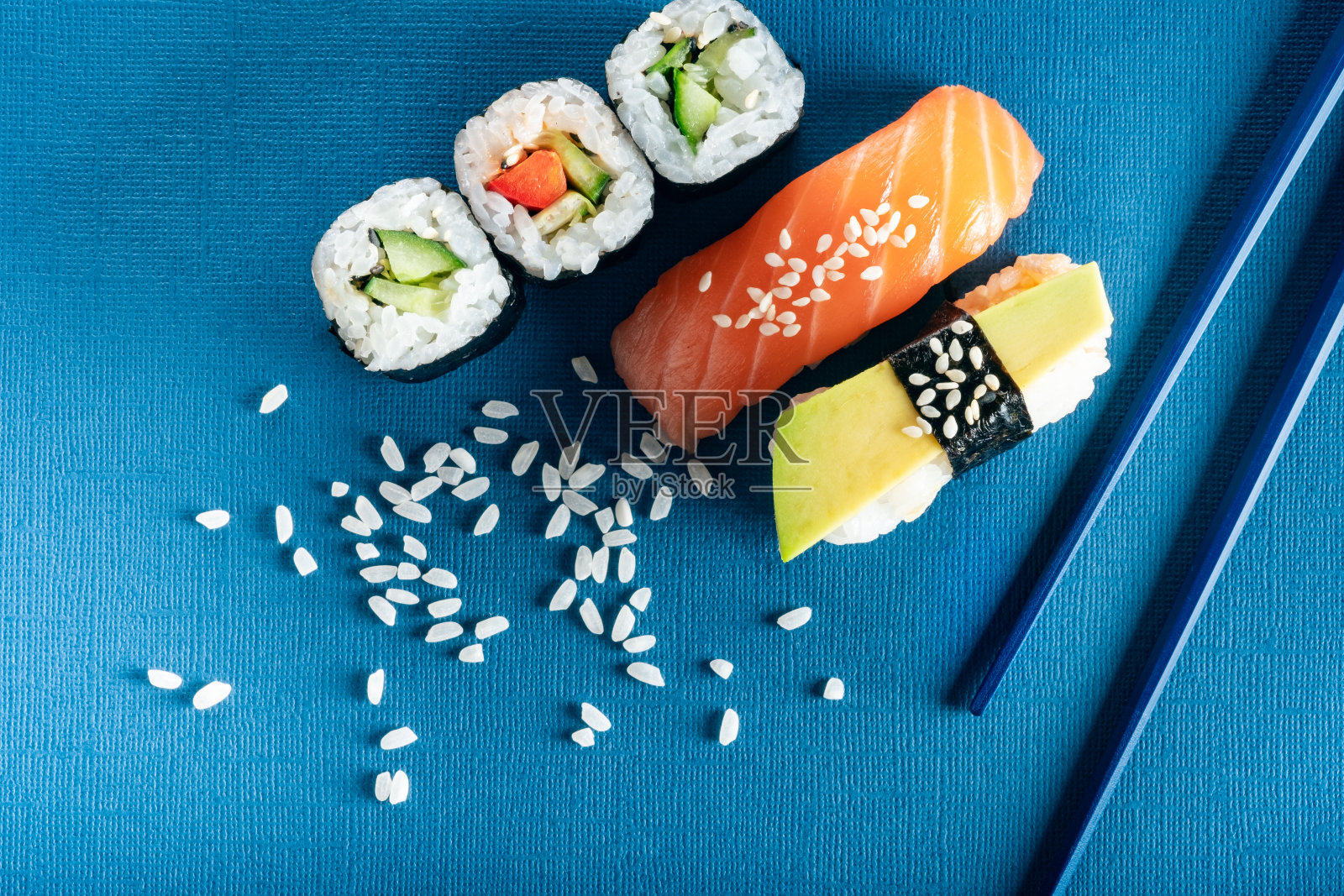 一套寿司和卷三文鱼，鳄梨和黄瓜在蓝色的背景和筷子，俯视图照片摄影图片