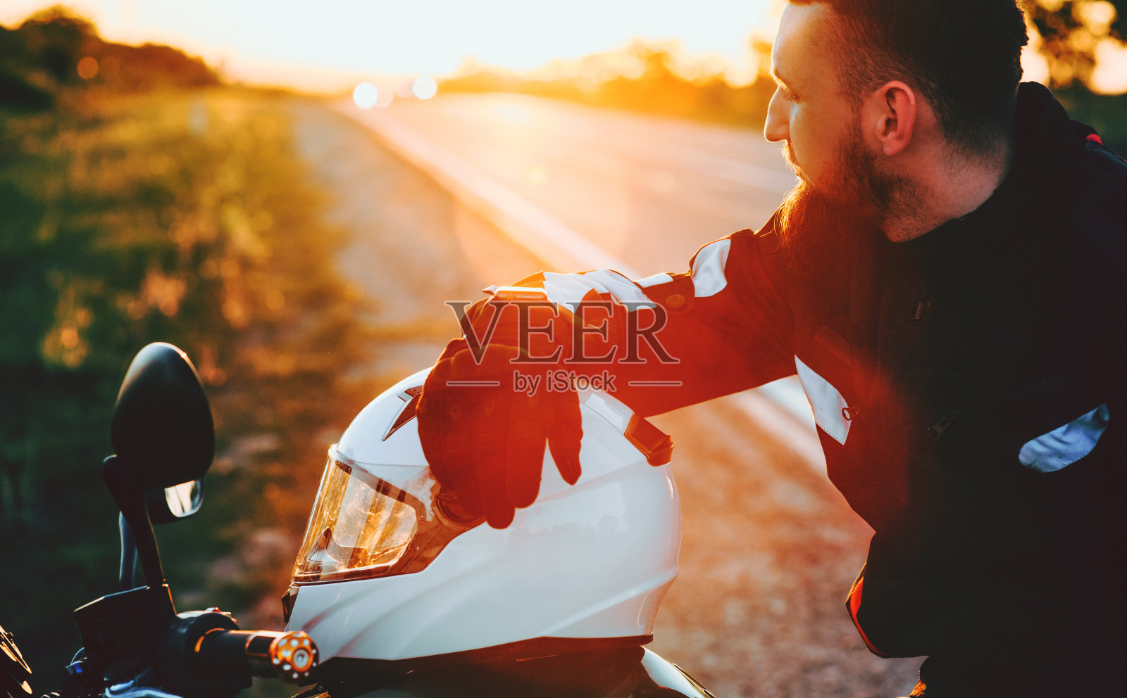 蓄着胡须的白人男孩在路边的摩托车上对着夕阳摆姿势，看着他前面的自然照片摄影图片