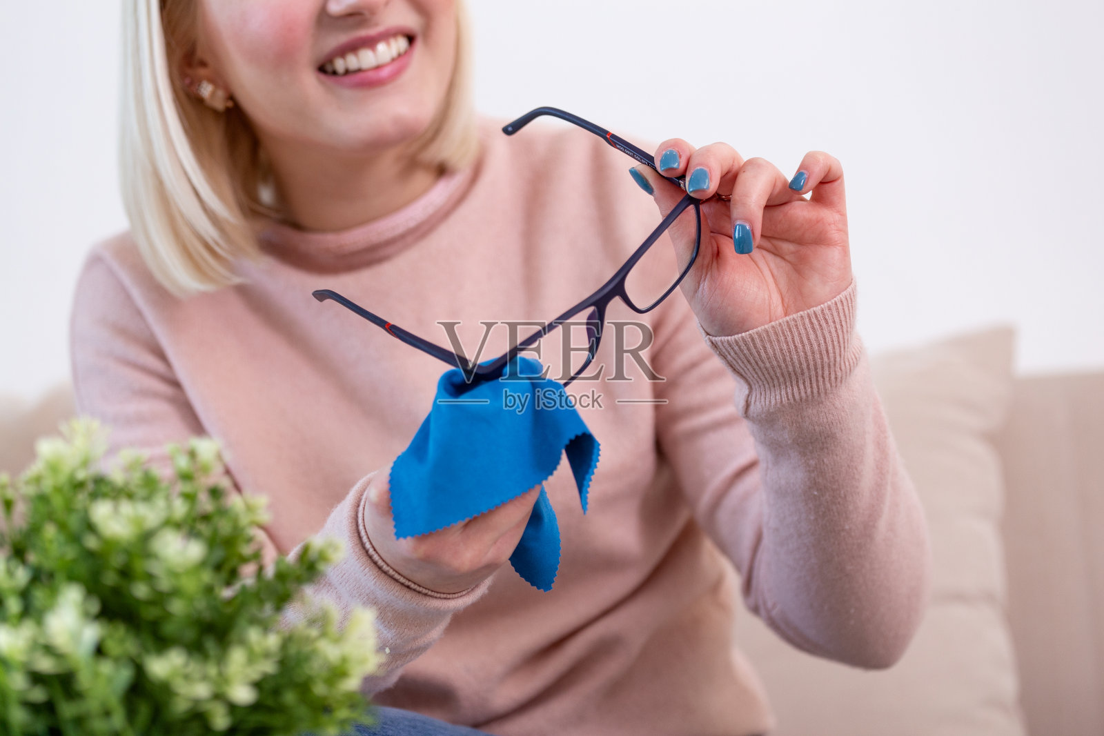 用布擦老花镜的女人。女人用蓝布手工清洁眼镜镜片。照片摄影图片