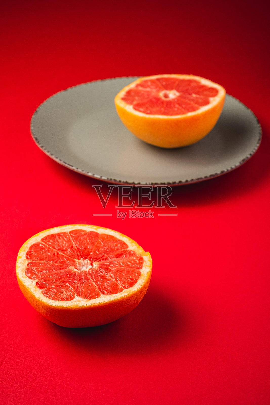 葡萄柚靠近灰色的盘子，水果的一半水果，热带创意简约的食物概念，在充满活力的红色背景，郁郁葱葱的熔岩，角度视角选择性焦点照片摄影图片