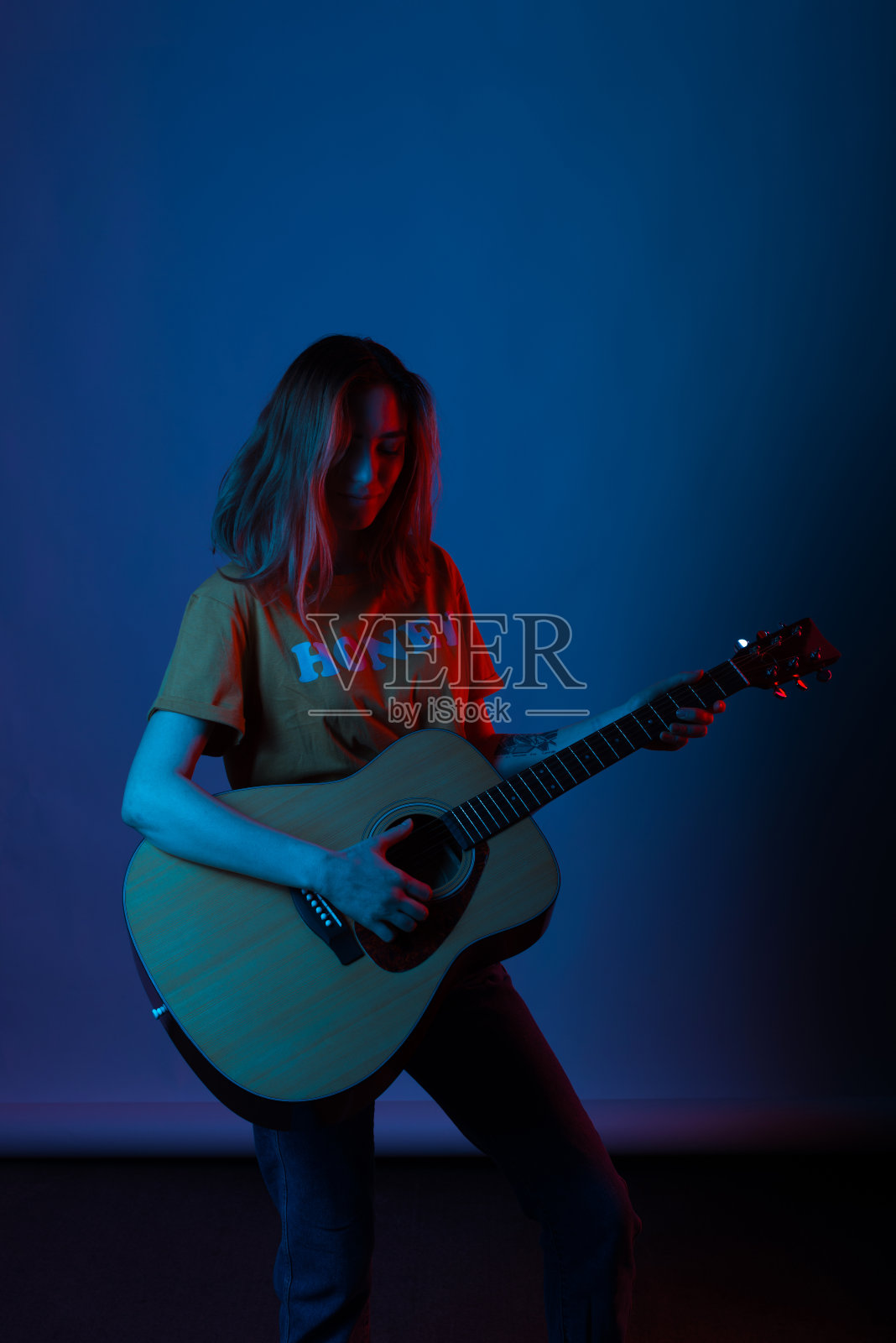 年轻女子在蓝色背景和一些红色灯光下弹吉他。照片摄影图片