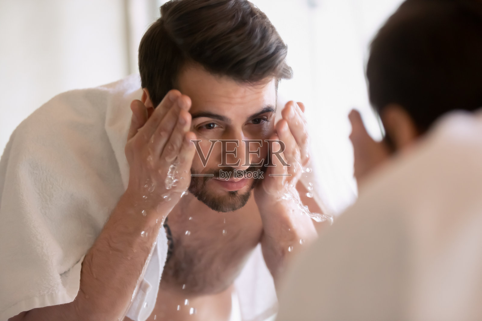 年轻人在浴室里洗脸，看着镜子照片摄影图片