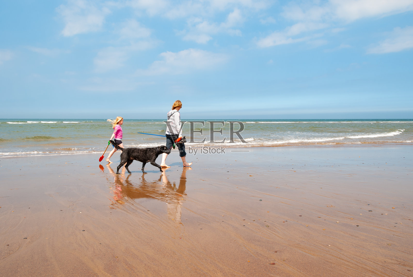 妈妈和女儿沿着沙滩海岸线遛狗照片摄影图片