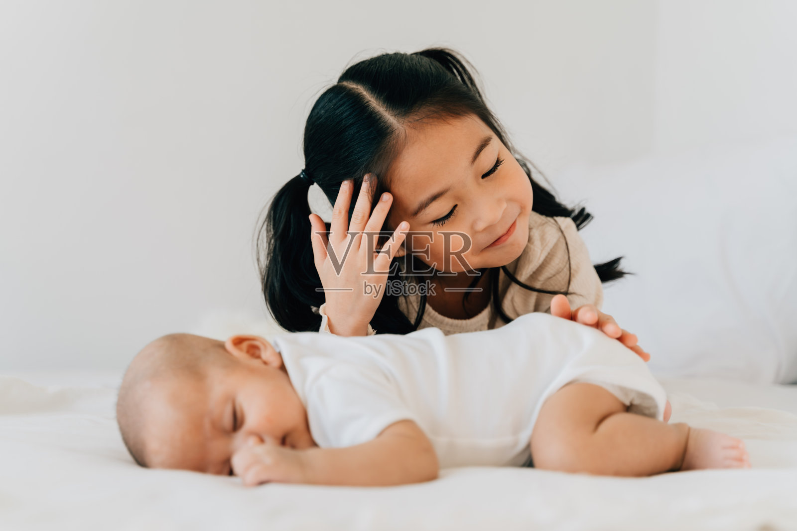 亚洲家庭可爱的小妹妹触摸新生的男孩弟弟。蹒跚学步的孩子和刚出生的兄弟姐妹在家里的白色卧室里放松照片摄影图片