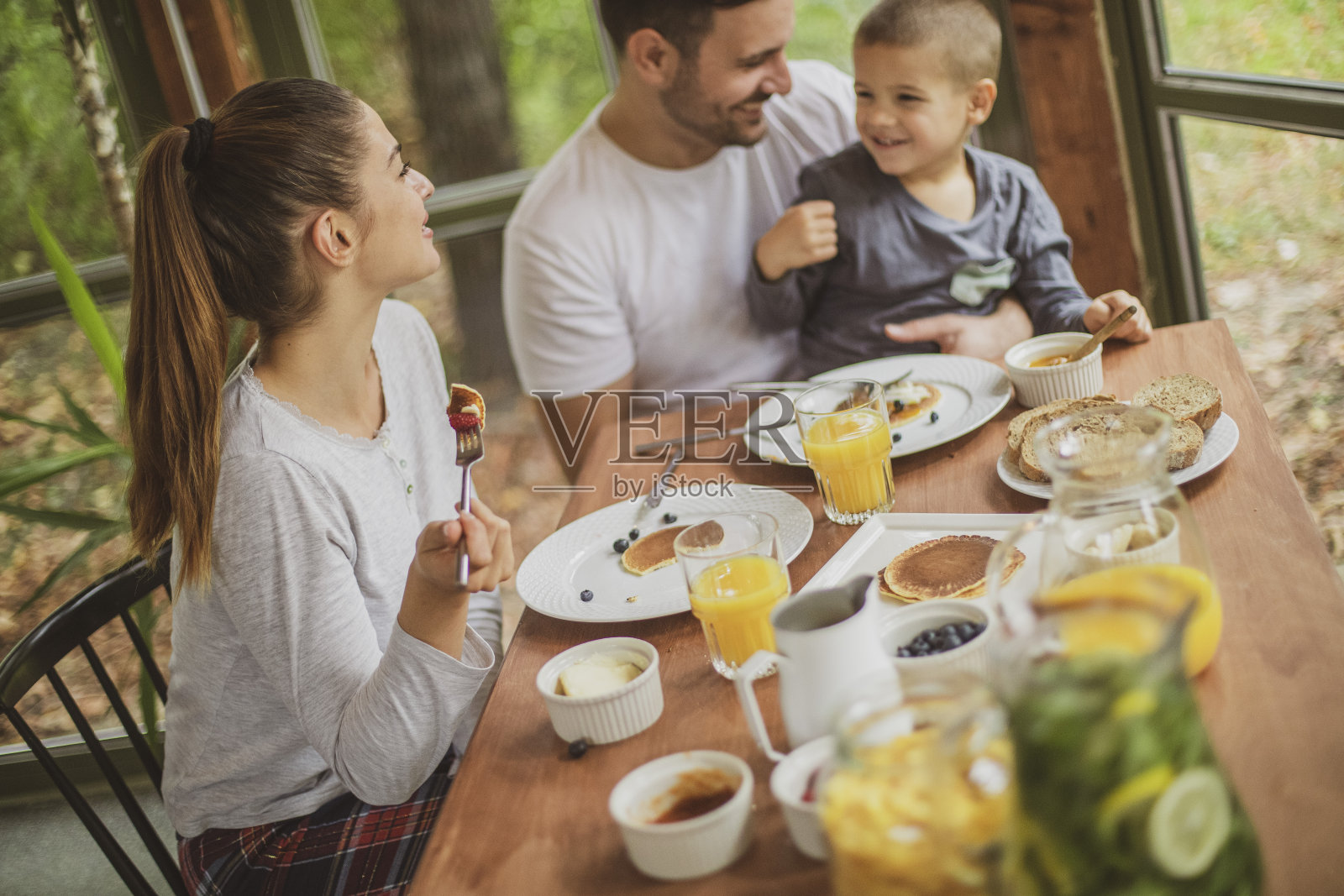 一个年轻的家庭穿着他们的睡衣在一个舒适的小木屋在树林里吃健康的早餐。照片摄影图片