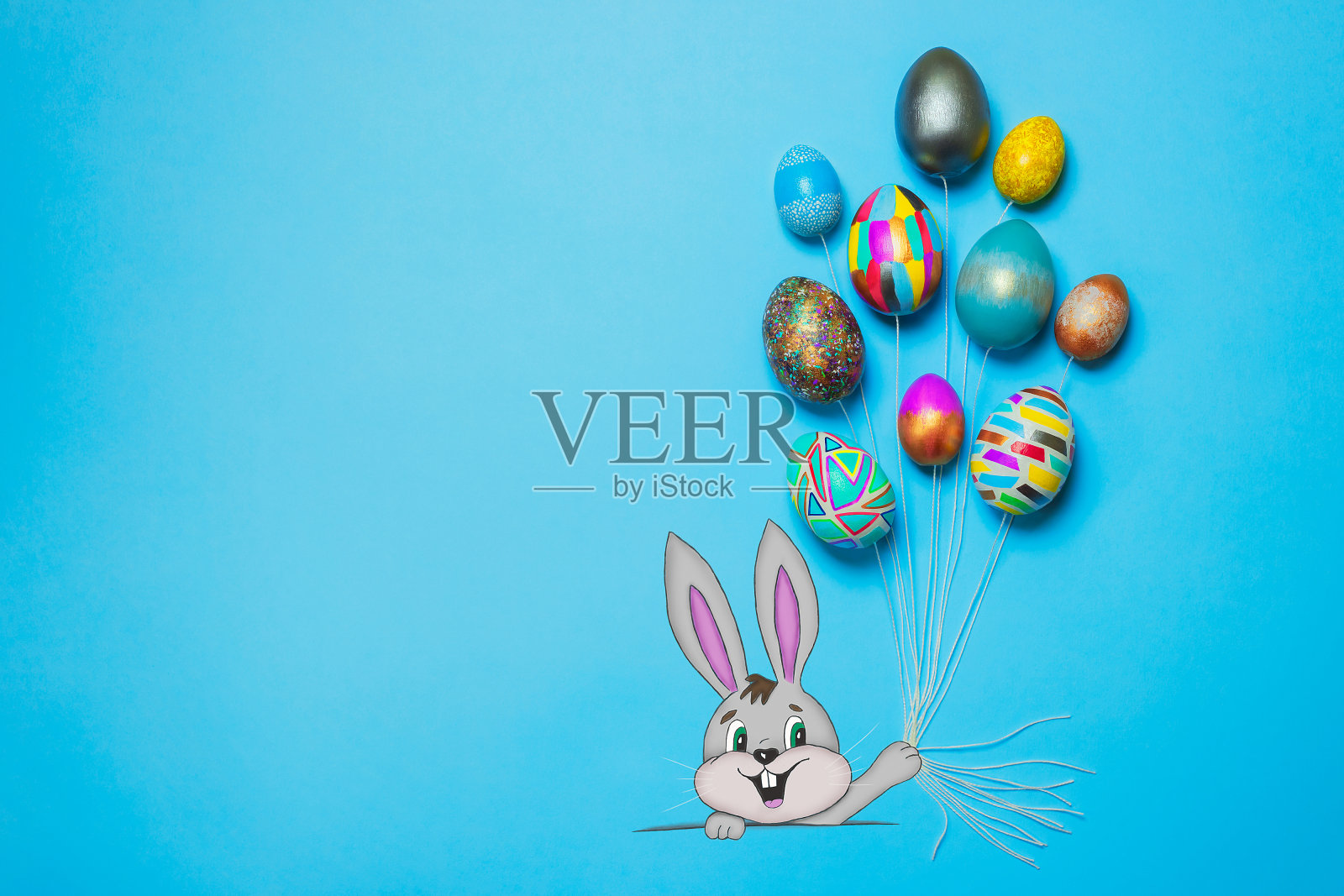 微笑的卡通兔子拿着彩绘成气球形状的复活节彩蛋。复活节快乐的概念。亮蓝色背景，俯视图，拷贝空间，横幅插画图片素材