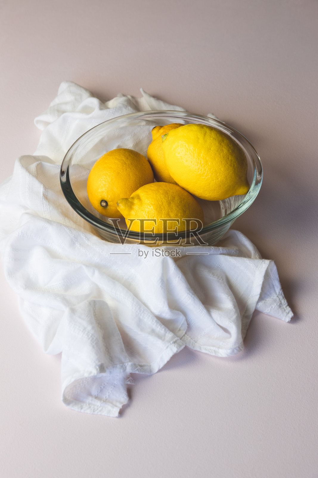 玻璃碗里的柠檬，周围是白色的棉花帘子，背景是淡粉色照片摄影图片