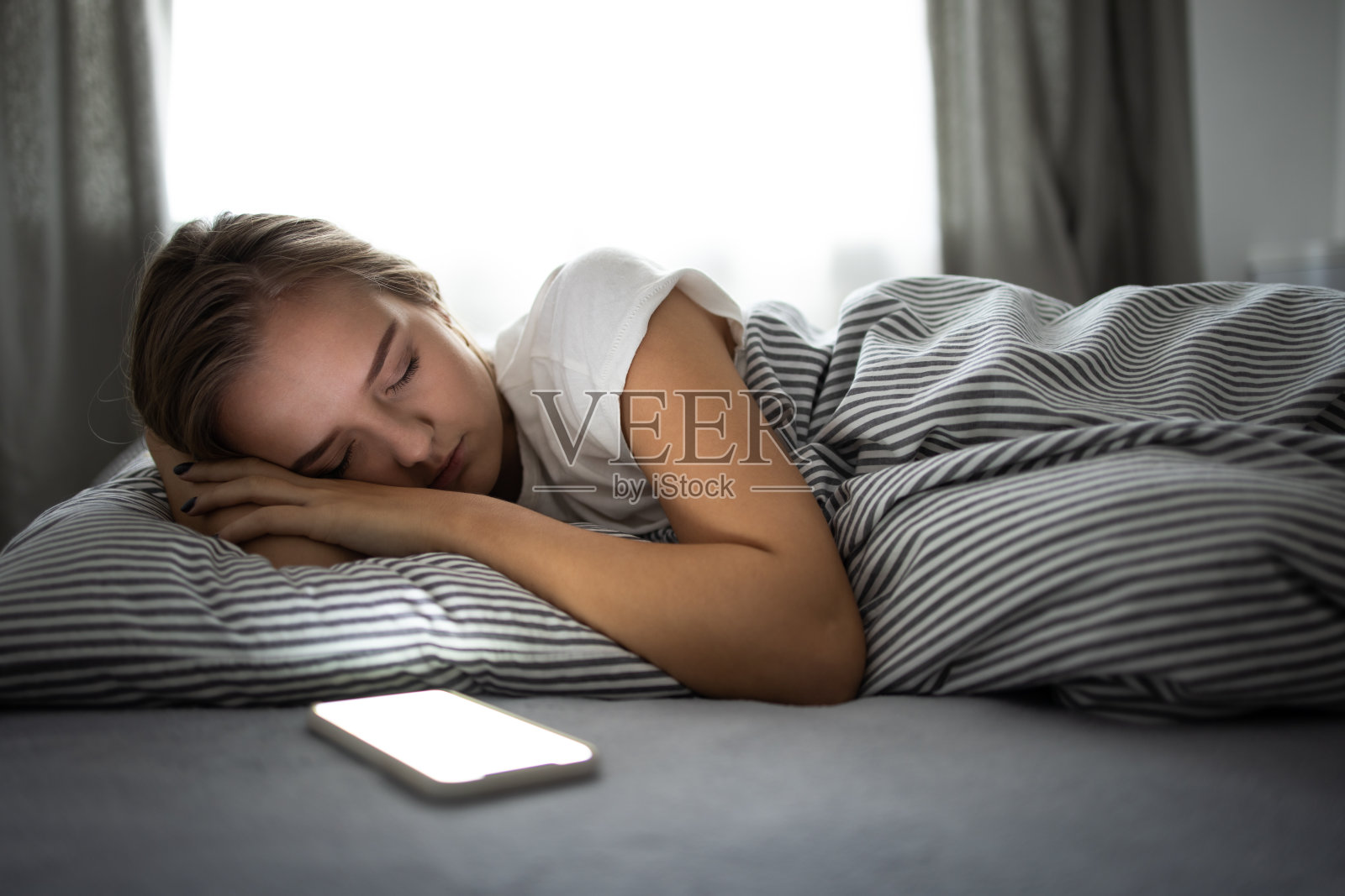 睡在床上拿着手机的漂亮年轻女人照片摄影图片