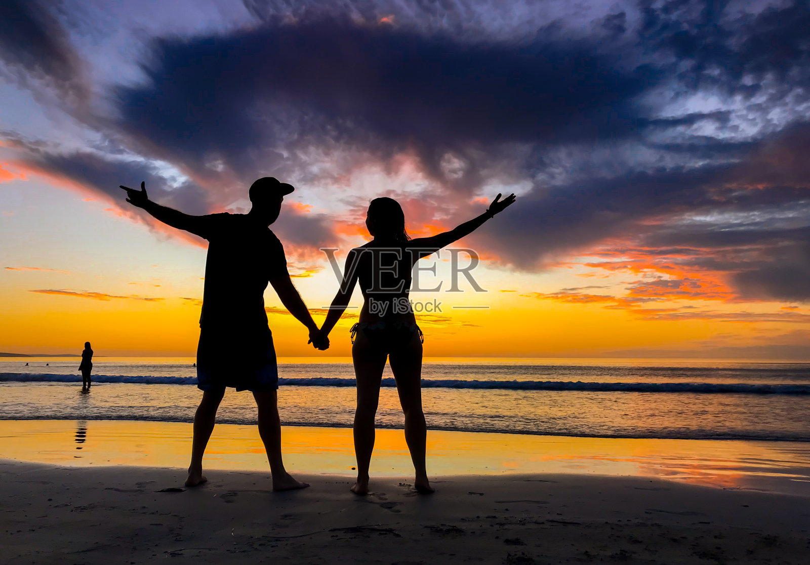 情侣的剪影在蜜月期间在壮观的海滩日落感觉自由。男人和女人剪影庆祝爱、自由和健康。浪漫逃离了假期和健康的概念。照片摄影图片