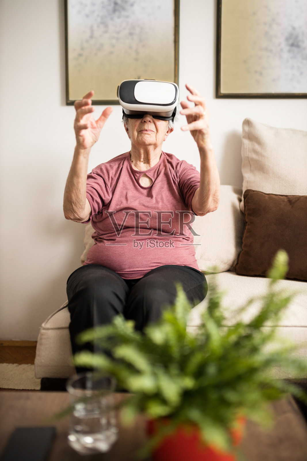 一位资深女性坐在客厅的沙发上，戴着虚拟现实模拟器眼镜照片摄影图片