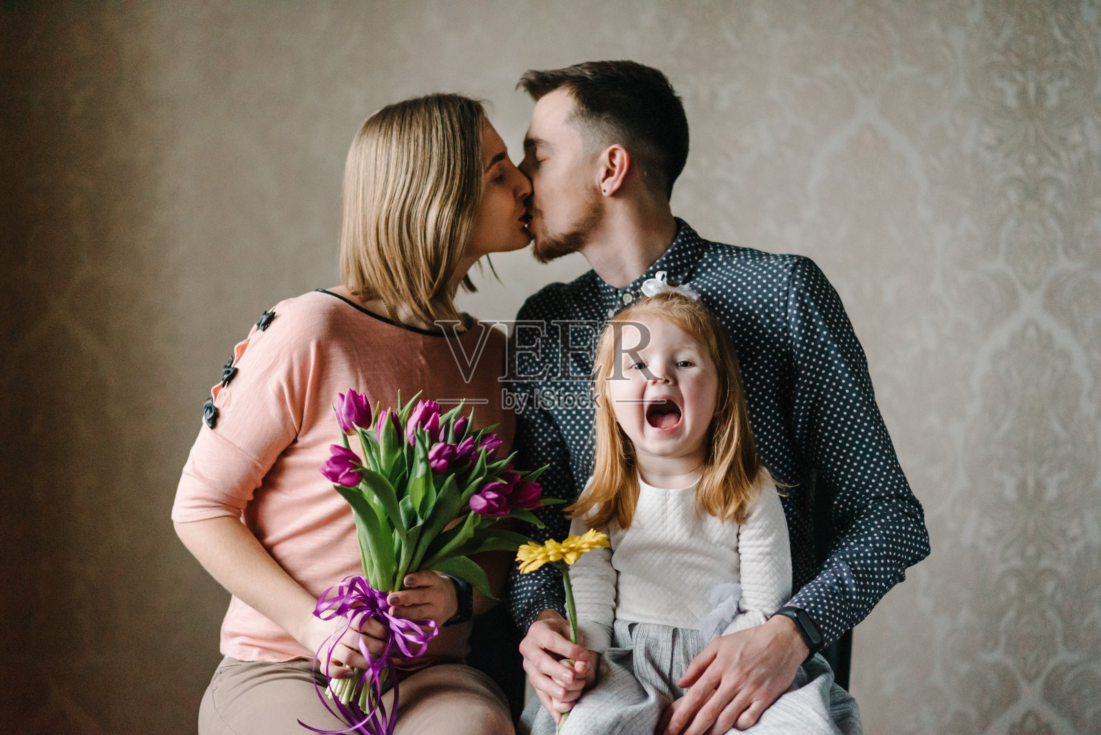 母亲节快乐!女儿带着爸爸祝贺妈妈，并送给她郁金香花。妈妈，爸爸亲吻和拥抱。家庭假期和团聚。国际妇女节。照片摄影图片