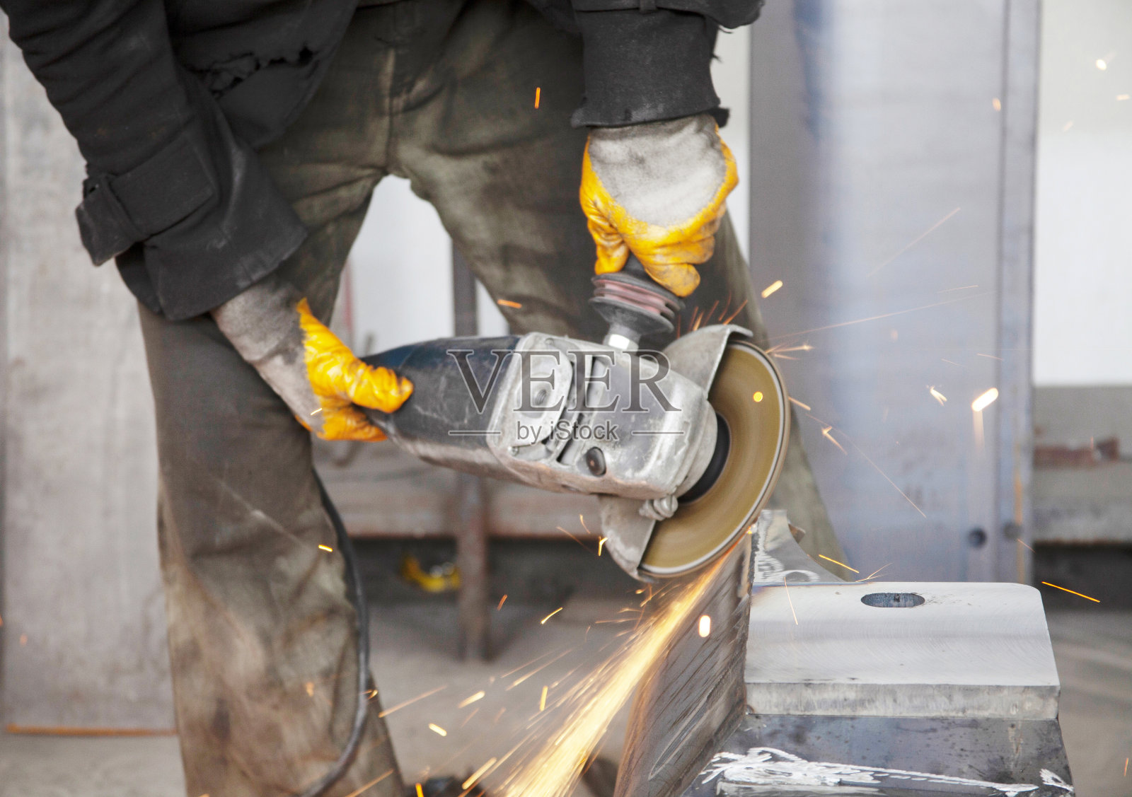 重工业工人用角磨床切割钢材。电动研磨机。照片摄影图片