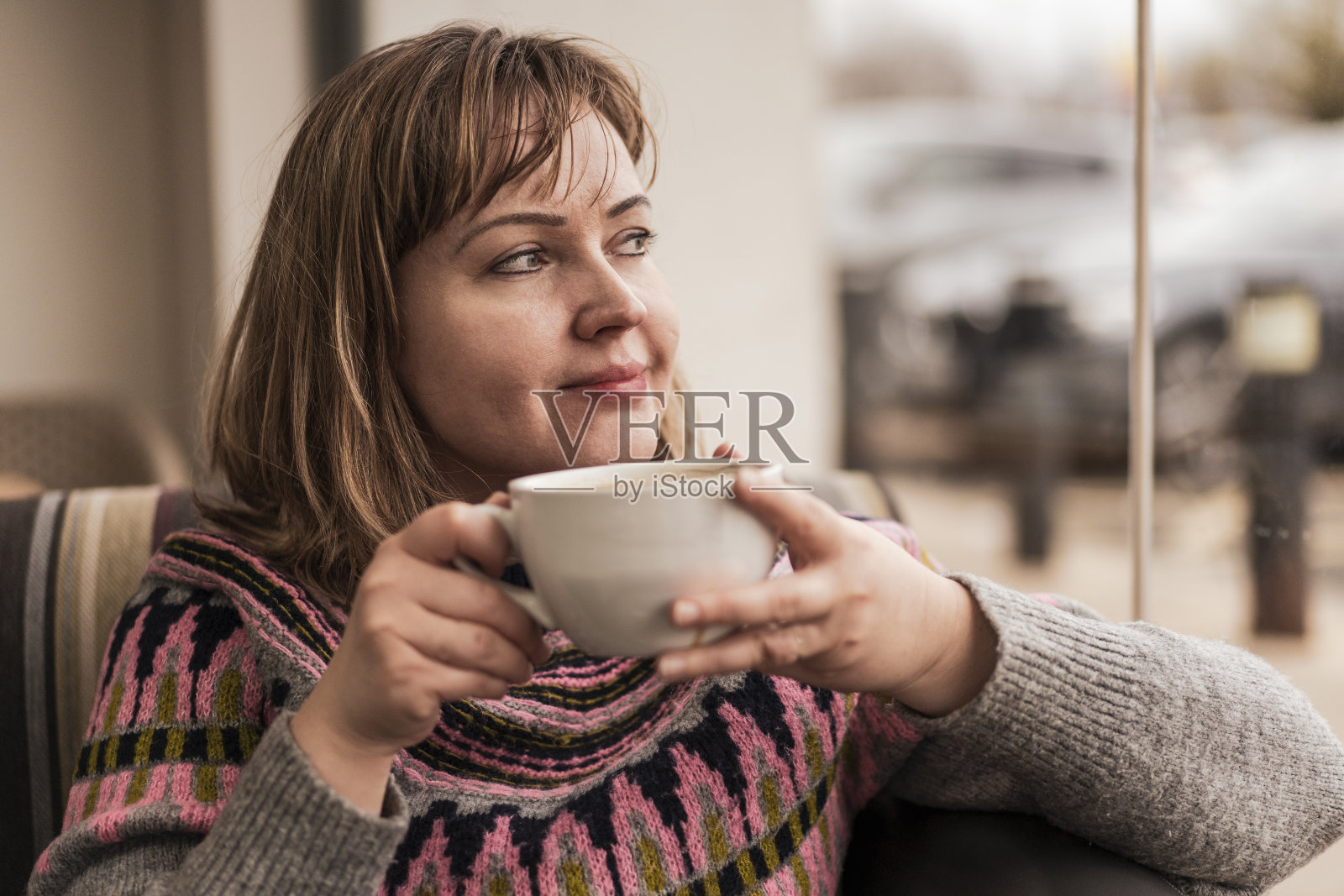 年轻微笑的女人拿着一杯拿铁咖啡近距离的一个女人拿着一杯咖啡的女人与床上的咖啡手坐在床上。年轻的黑发女子享受一杯拿铁卡布奇诺咖啡照片摄影图片