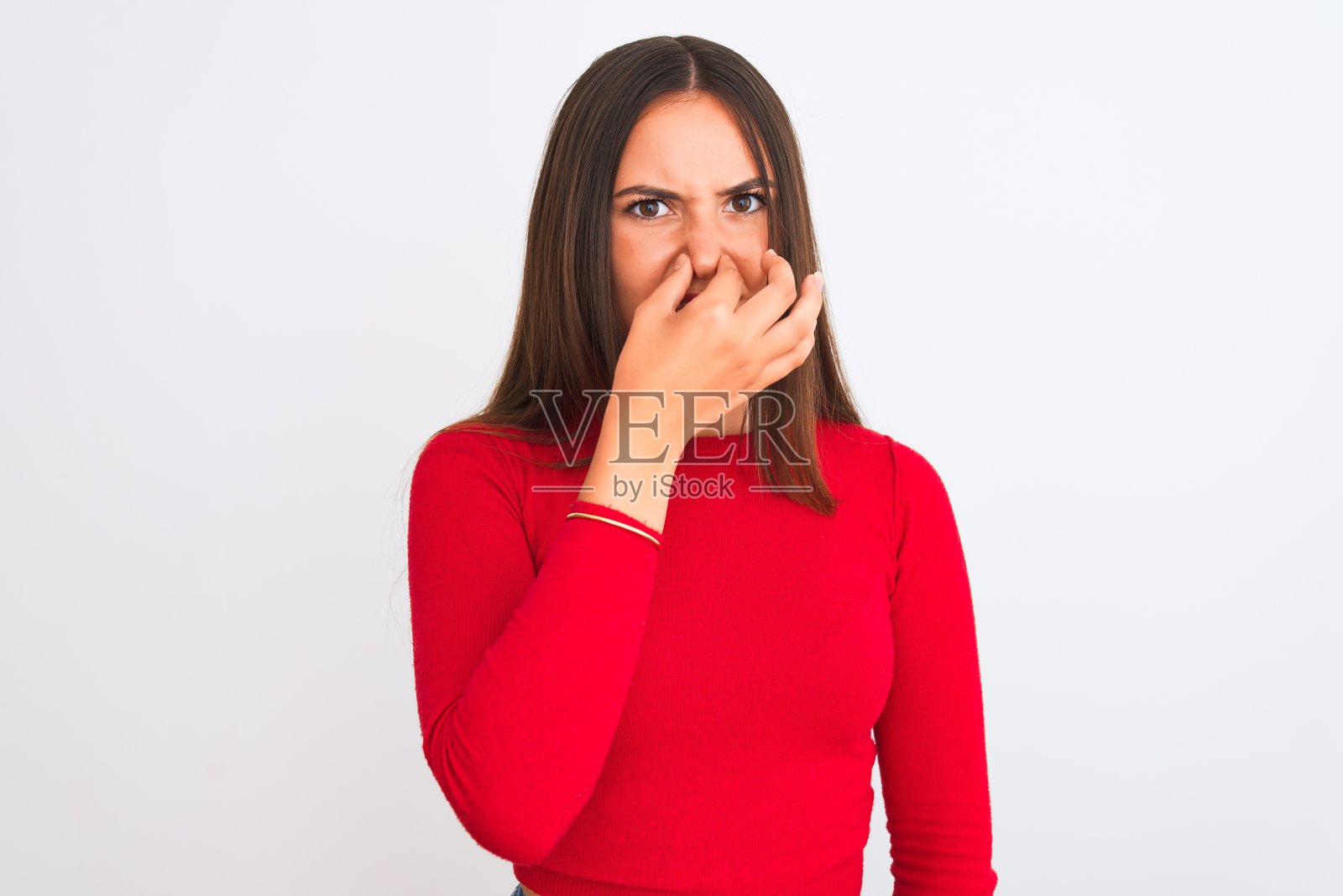 年轻美丽的女孩穿着红色休闲t恤站在孤立的白色背景闻一些臭气和恶心，难以忍受的气味，屏住呼吸用手指在鼻子上。“坏味道”的概念。照片摄影图片