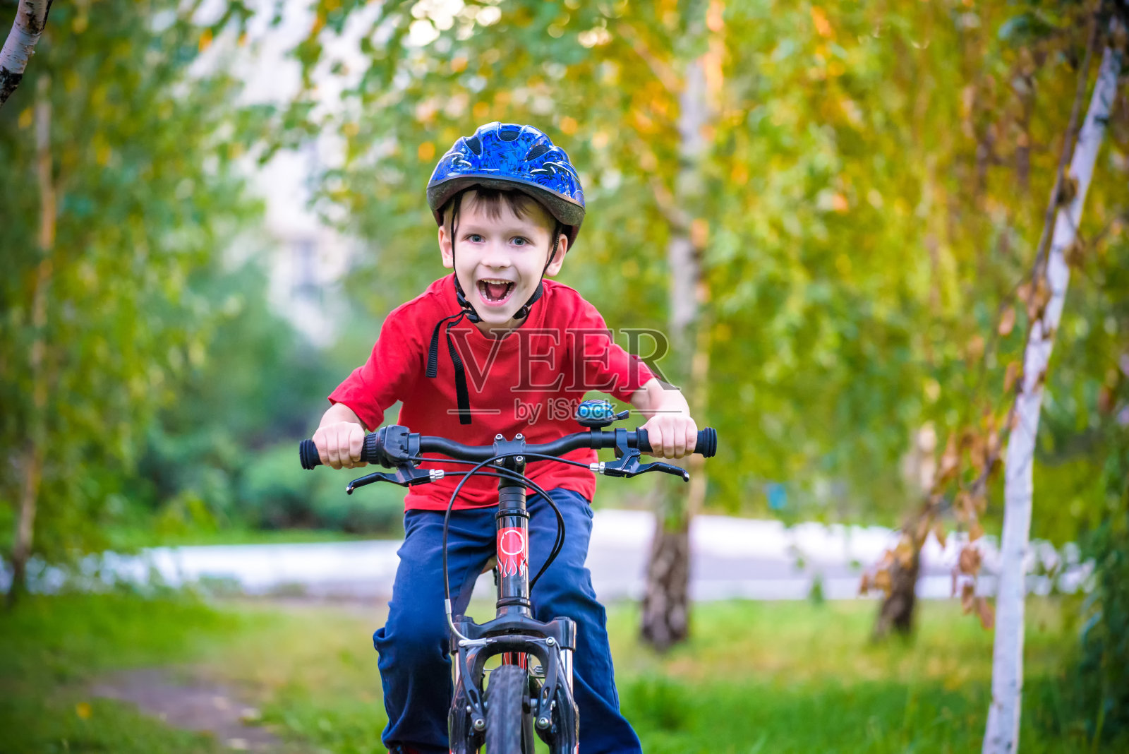 一个戴着防护头盔的白色小男孩坐在一辆儿童自行车上。蹒跚学步的孩子骑着红色两轮自行车朝前看。孩子脸上露出狡黠的微笑照片摄影图片