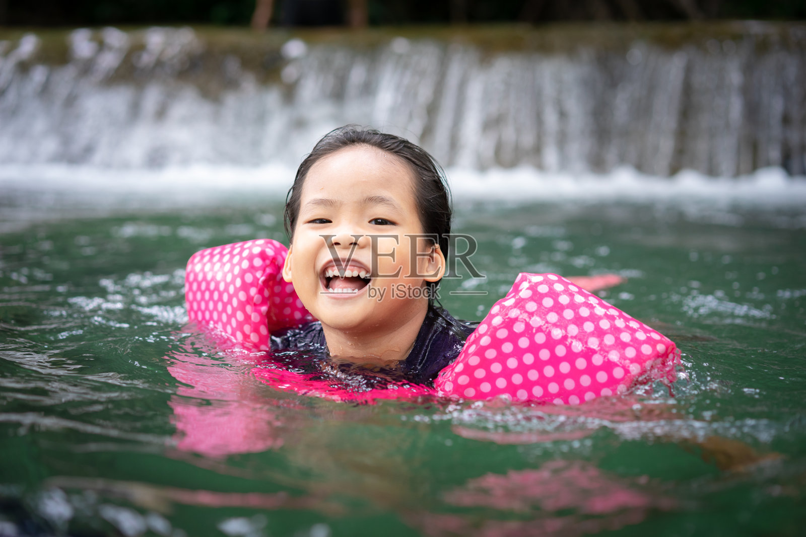 亚洲小女孩穿着充气的袖子在自然的水里游泳度假照片摄影图片