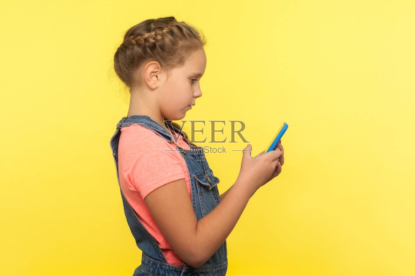 侧面的严肃可爱的小女孩在手机上专心阅读信息，在社交网络上聊天照片摄影图片
