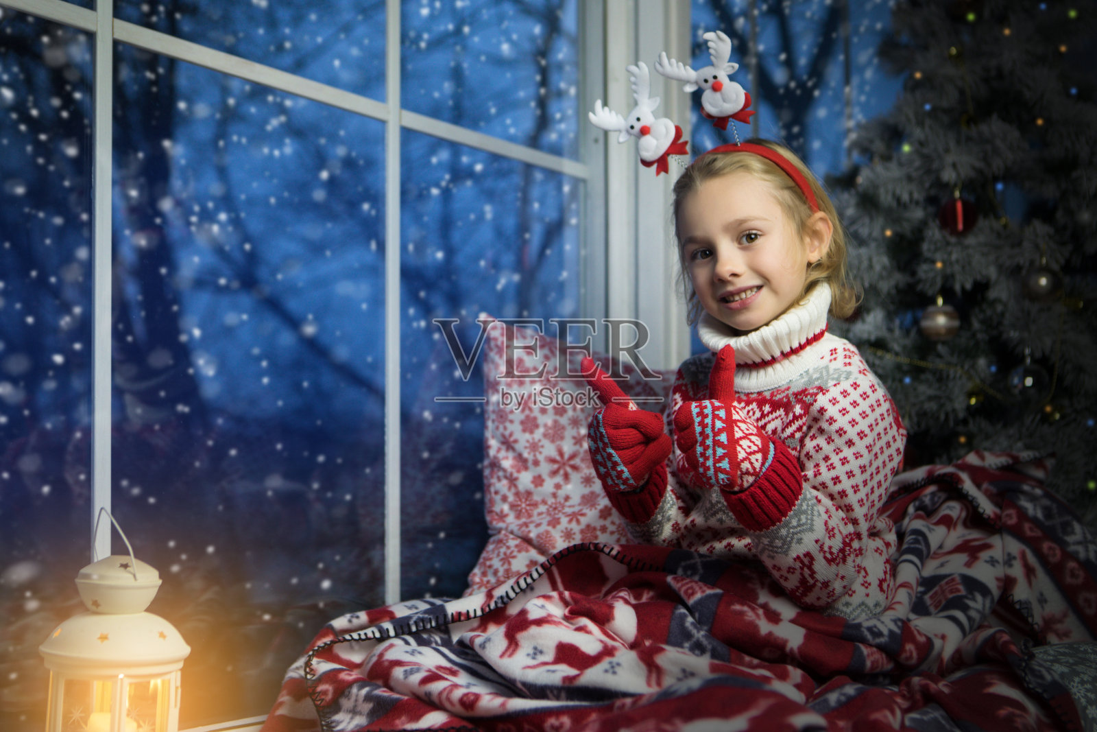 小女孩坐在窗前和圣诞树旁照片摄影图片
