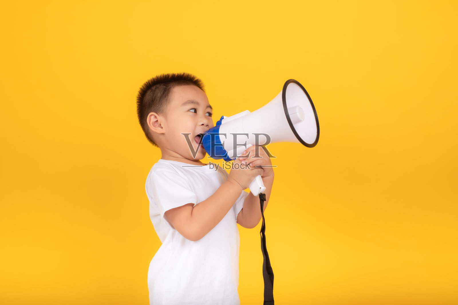 快乐的小亚洲儿童男孩微笑着用扩音器宣布打折销售，夏天的声音叫穿着白色的t恤棉布在黄色的背景孤立摄影棚拍摄，复制空间。照片摄影图片