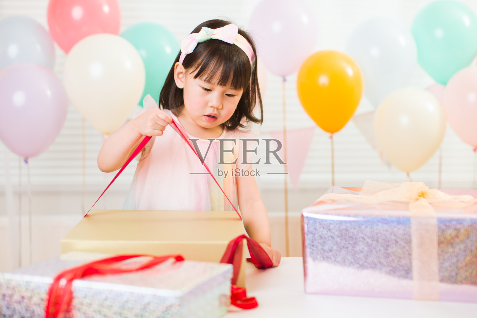 蹒跚学步的小女孩在她的生日派对上打开生日礼盒照片摄影图片