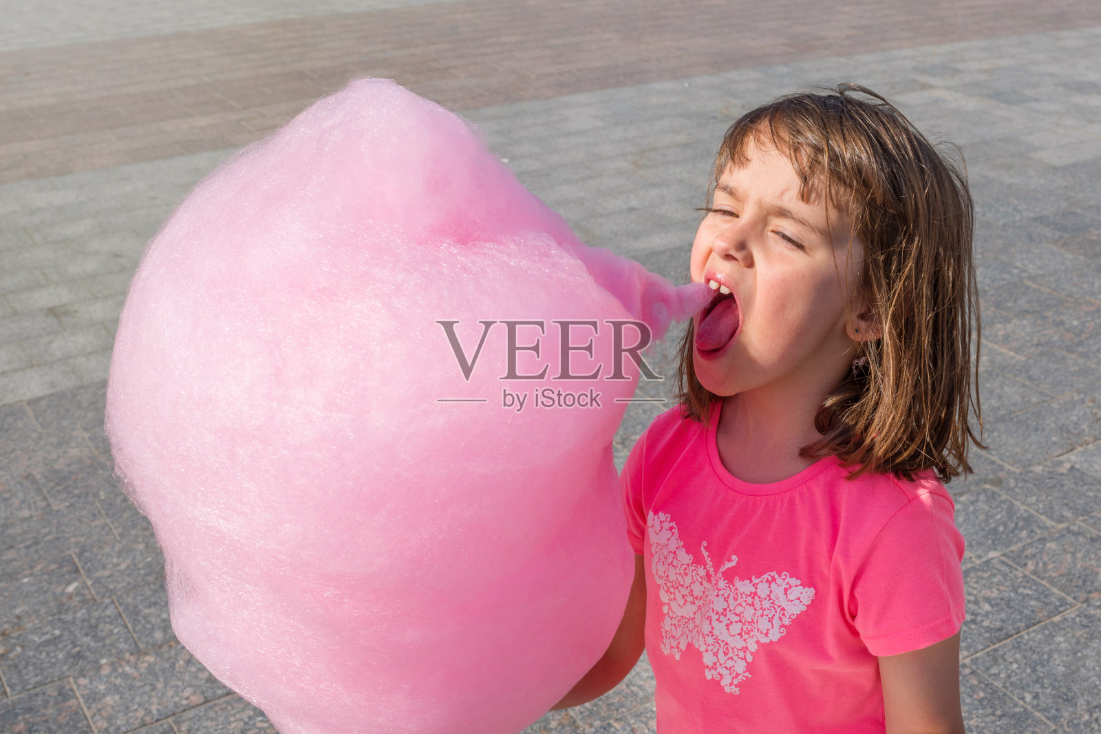 一个可爱的孩子在阳光明媚的日子里吃着粉红色的糖精棉絮。糖果。照片摄影图片