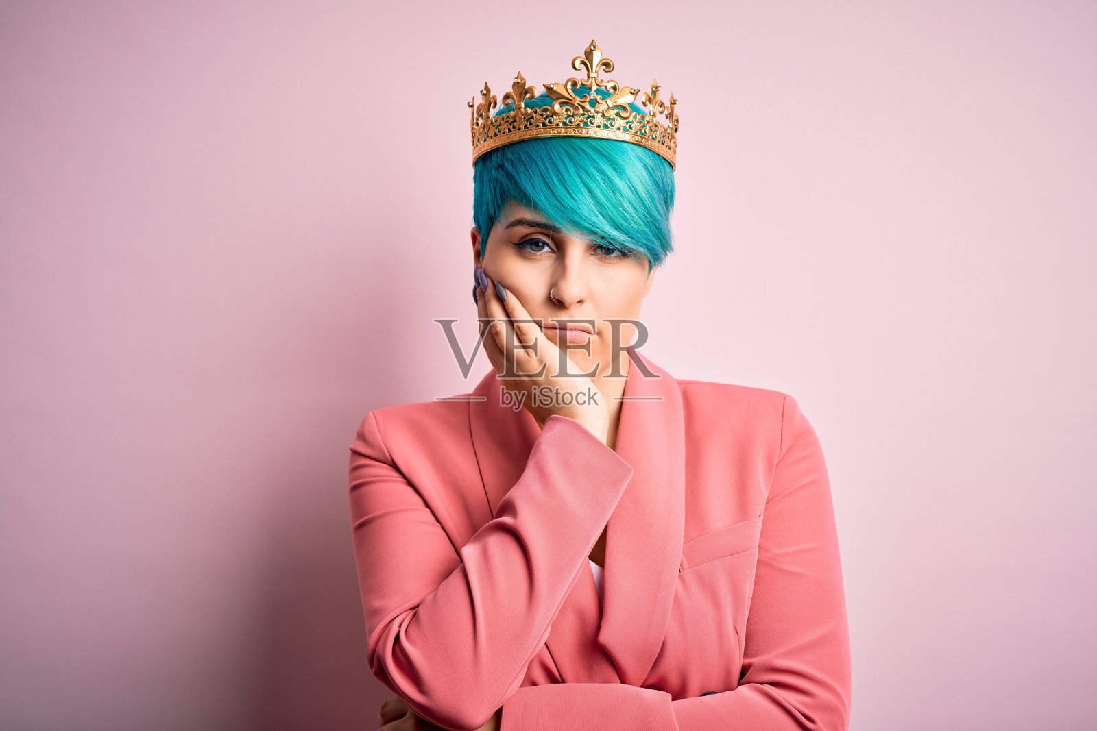 年轻的商业女性与蓝色时尚的头发戴女王皇冠在粉红色孤立的背景思考看起来疲倦和厌倦抑郁症的问题交叉双臂。照片摄影图片