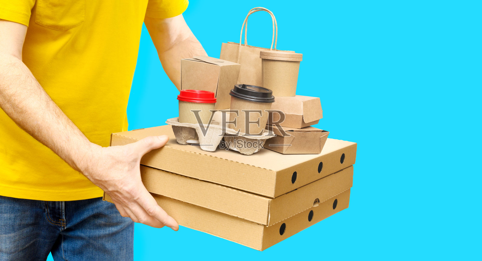 黄色衬衫的送货员拿着各种外卖食品容器、披萨盒、咖啡杯和蓝色背景的纸袋。本空间照片摄影图片