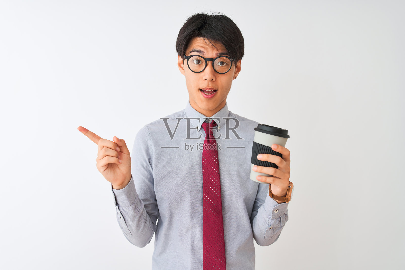 中国商人戴着领带和眼镜，在孤立的白色背景下喝咖啡，非常高兴地用手和手指指着一边照片摄影图片
