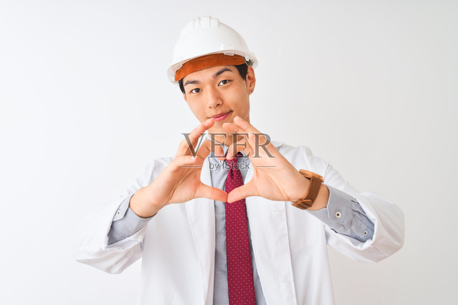中国建筑师穿着外套和头盔站在孤立的白色背景微笑在爱显示心形符号和形状的手。浪漫的概念。照片摄影图片