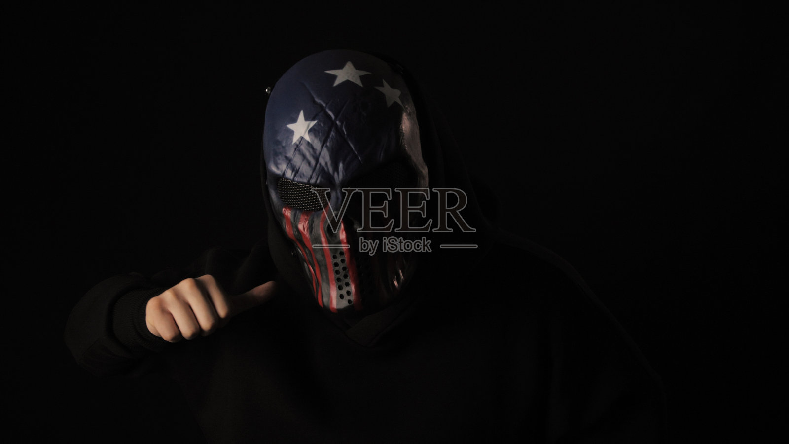 一个人戴着一个可怕的美国国旗颜色的面具，显示了一个死亡的手势照片摄影图片