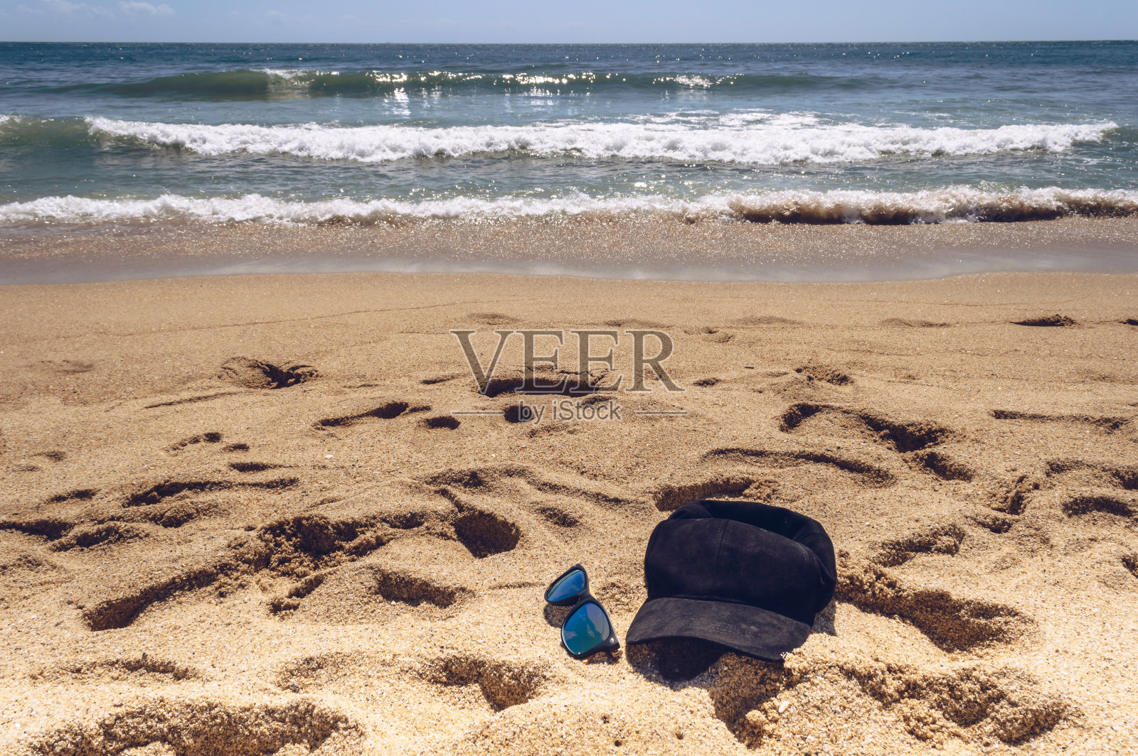 在阳光明媚的日子里，在海滩上戴着棒球帽和太阳镜照片摄影图片