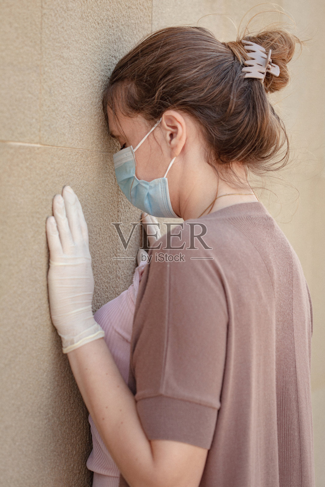 一名焦虑的妇女在COVID-19大流行期间戴着防护口罩，面朝墙壁照片摄影图片