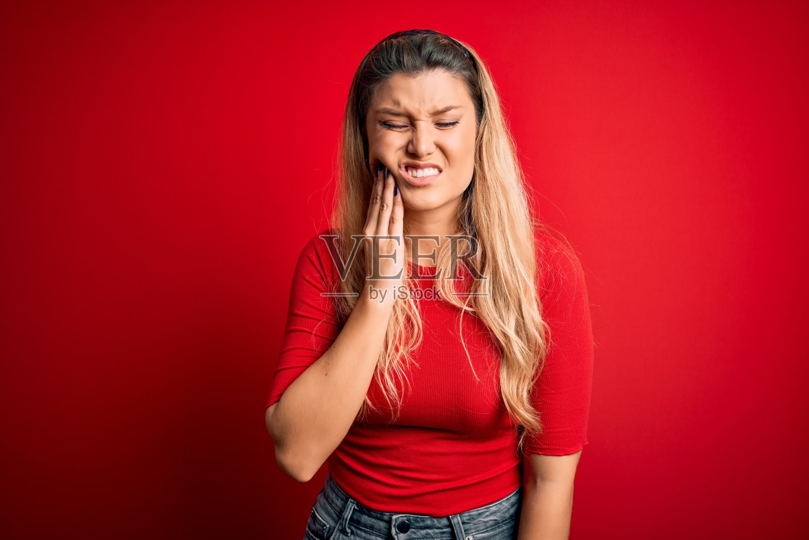 年轻美丽的金发女人穿着休闲t恤站在孤立的红色背景触摸嘴与手痛苦的表情，因为牙痛或牙齿疾病的牙齿。牙医照片摄影图片