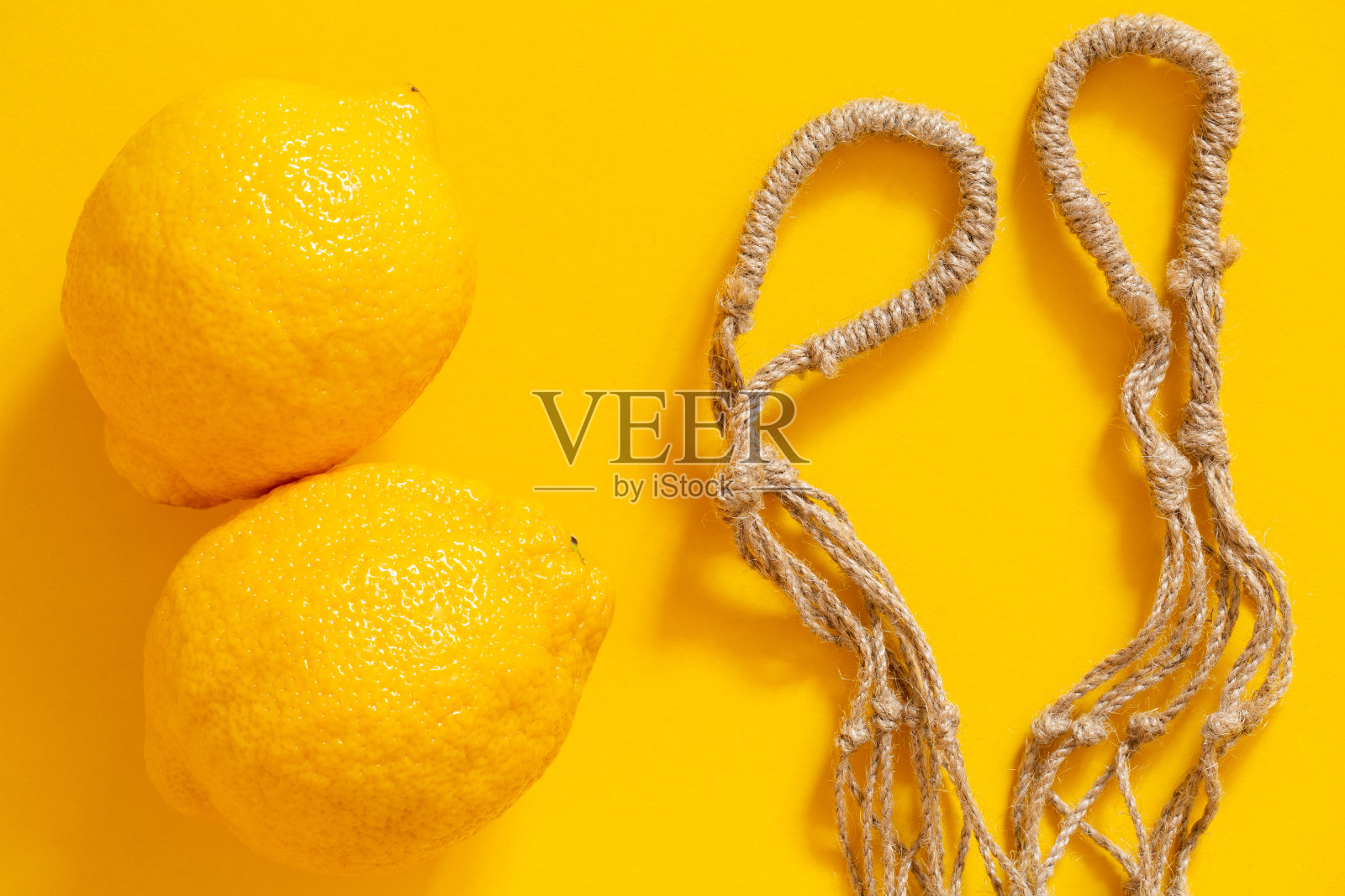 黄色背景上的网袋和柠檬。照片摄影图片
